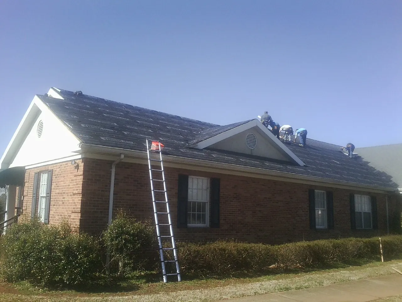Crew tearing shingles off a brick ranch roof with a ladder set — Metal Roof Repair work by our crew in Mountain City
