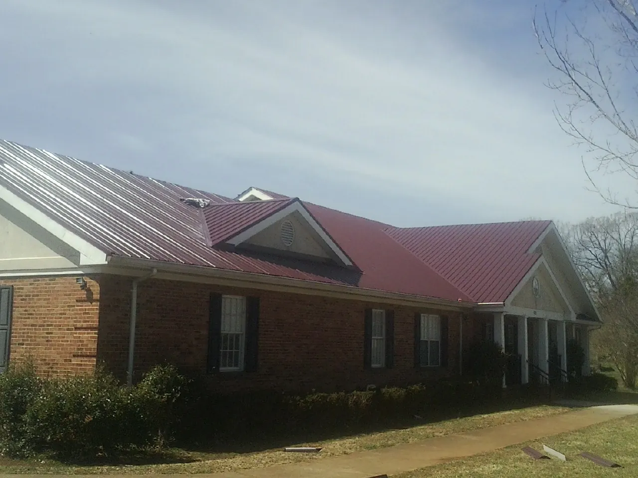 Red metal roof with gabled entries on a long brick building, from a Hail Damage Roof Repair job in Mountain City