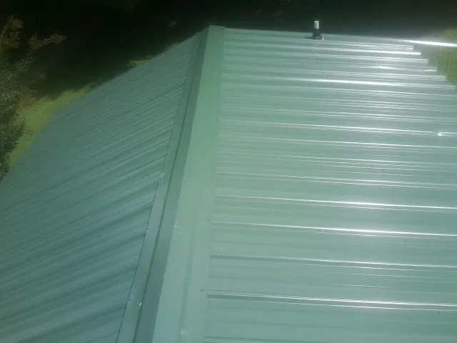 New green metal panels meeting at the ridge of a roof — Flat Roof Repair work by our crew in Mountain City