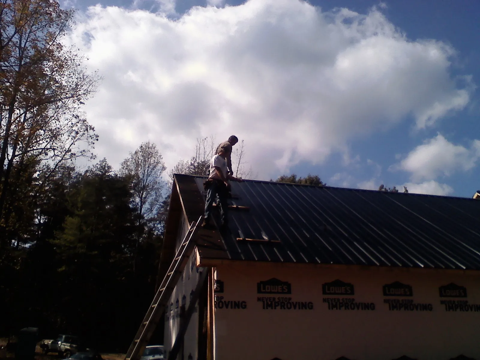 Roofer fastening dark metal panels high against a cloudy sky, from a Roof Inspection job in Mountain City