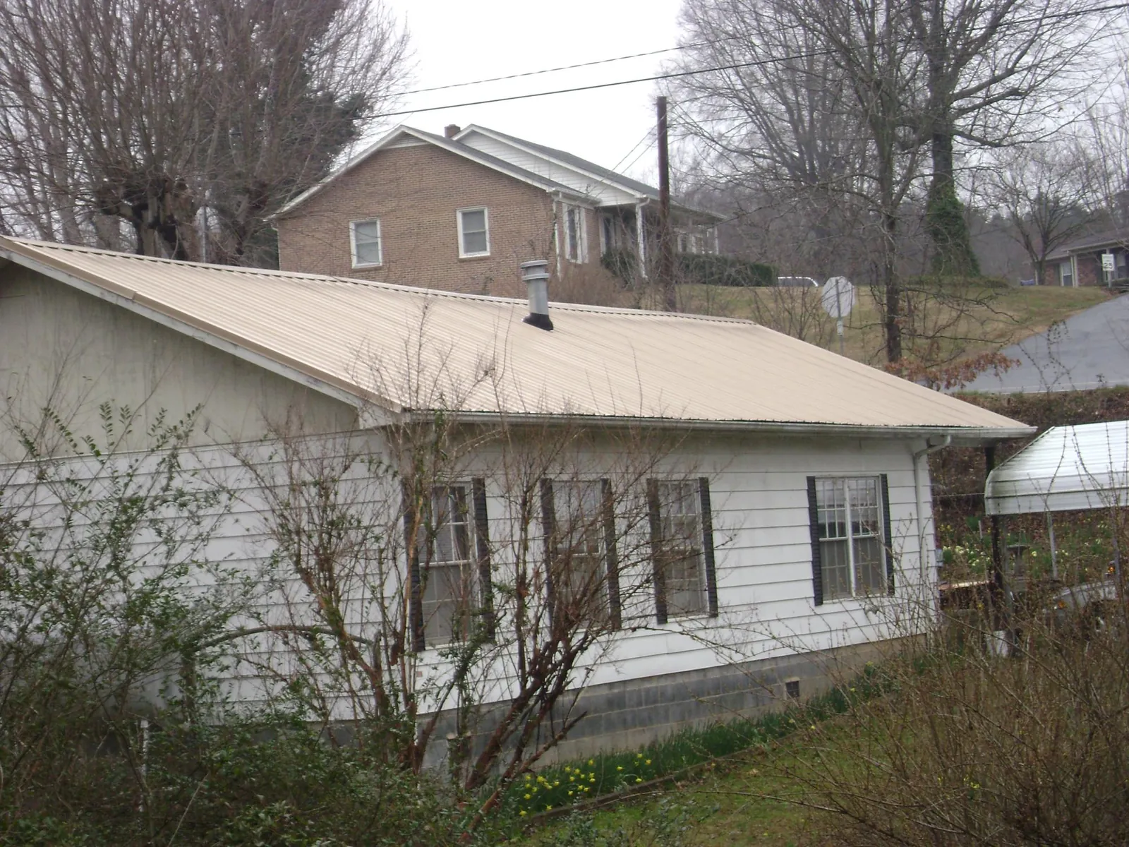 Tan metal roof on a white sided house set into a hillside — Commercial Roofing by Roofing Brothers in Mountain City